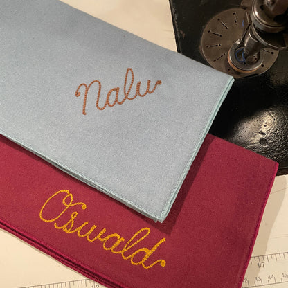 Two Dog Bandanas with chain stitched embroidered names on a surface with a chain stitching machine in the background